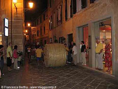 Night in the old town: people run along cobbled street pushing a giant roll