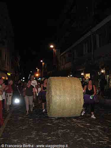 People push a giant hay bale along the street at night