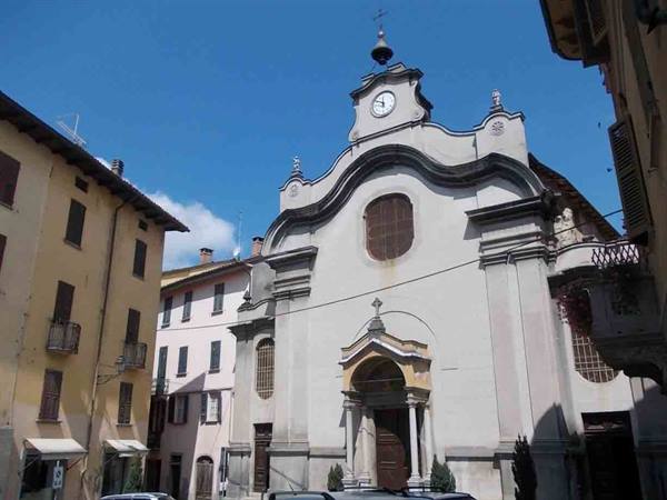 White church with curved facade, clock and bell tower, among colorful houses under blue sky