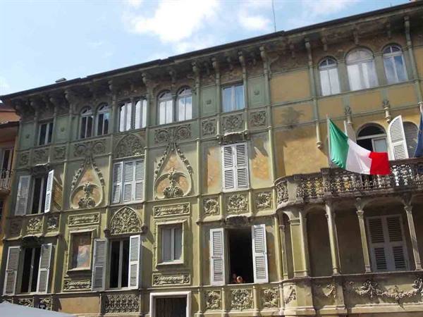 Liberty-style facade with green stucco, iron balcony and Italian flag in sunlight