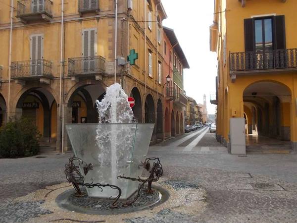 Glass fountain with water jet among arcades and ochre buildings