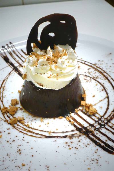 Chocolate dessert with whipped cream, crunchy disc and sauce on white plate
