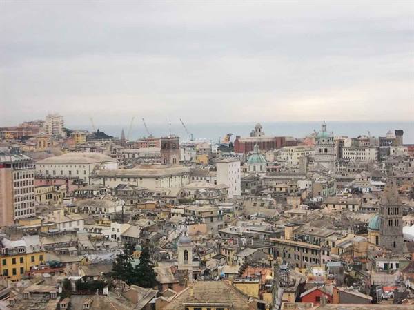 Genoa rooftops and domes under grey sky, sea in the distance