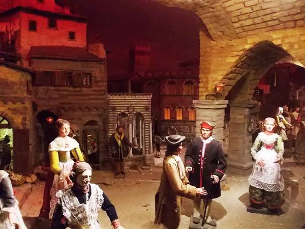 Diorama with figures in period costumes beneath stone arches, red lighting