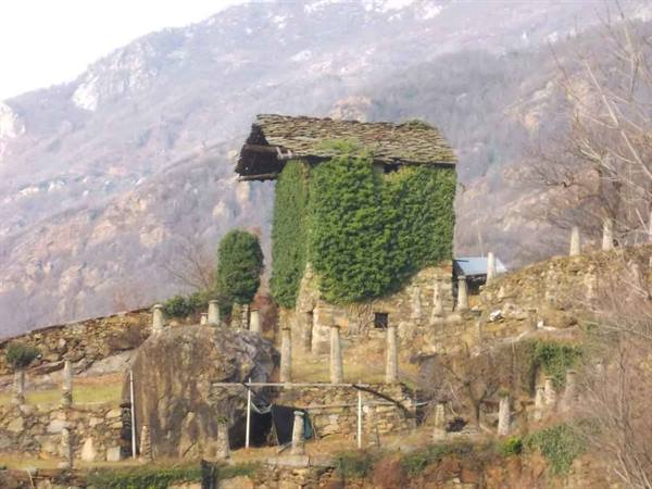 Ivy-covered stone hut with stone slab roof, mountains behind