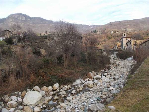 Dry stony streambed, village with bell tower and snowy mountains behind
