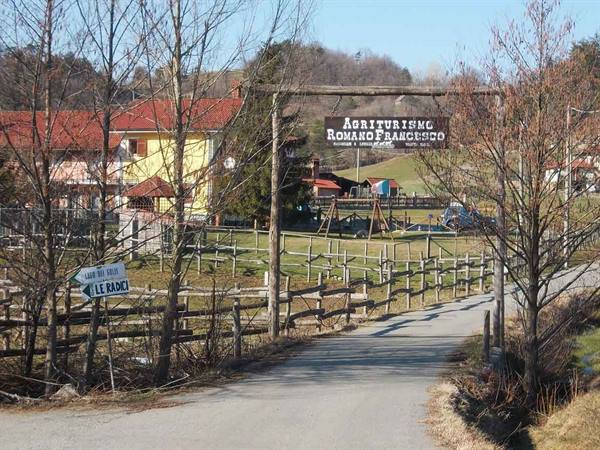Entrance to Romano Francesco farmhouse: wooden sign, timber fences, gravel road and rural houses