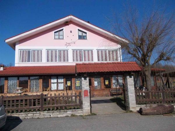 Pink farmhouse facade with tiled roof, wooden fence, blue sky