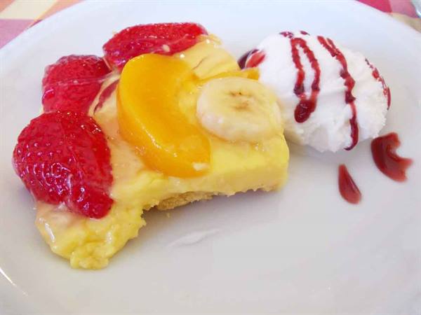 Italian custard tart with strawberries, peach and banana beside cream with strawberry sauce