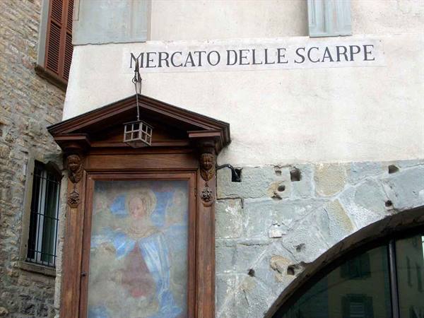 Wooden votive shrine with faded fresco beneath the shoe market sign