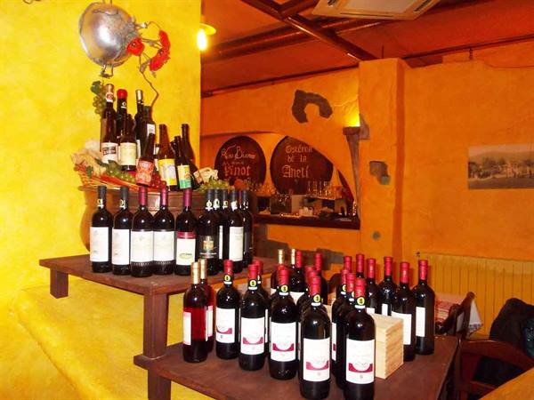 Red wine bottles on wooden tables inside a trattoria with yellow walls