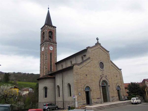 Stone church with brick bell tower and clock, parked cars under a cloudy sky