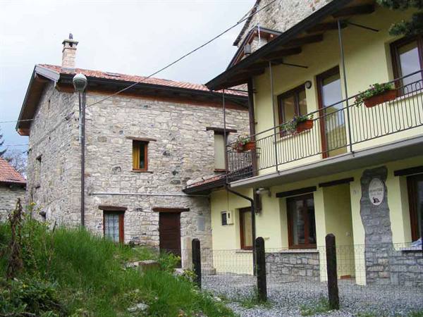 Stone house and yellow building with iron balcony, green garden