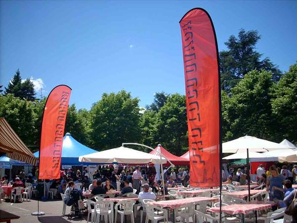 Orange feather banners over an open-air market with white umbrellas and tables