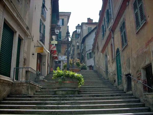 Stone staircase between old houses with green shutters, lanterns and flowers