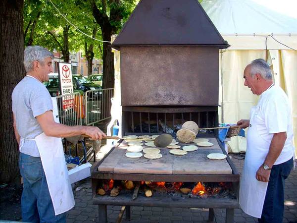 Two men baking flatbreads on stone slabs over fire beneath an iron hood