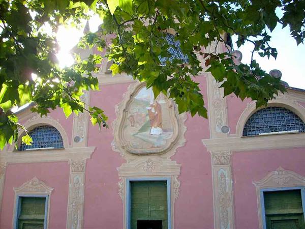 Pink church facade with fresco, green doors and windows framed by leaves