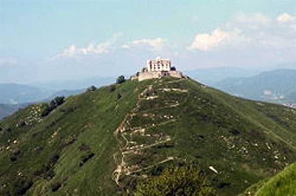 Old stone fortress on green hilltop, terraced trail climbing among Ligurian mountains