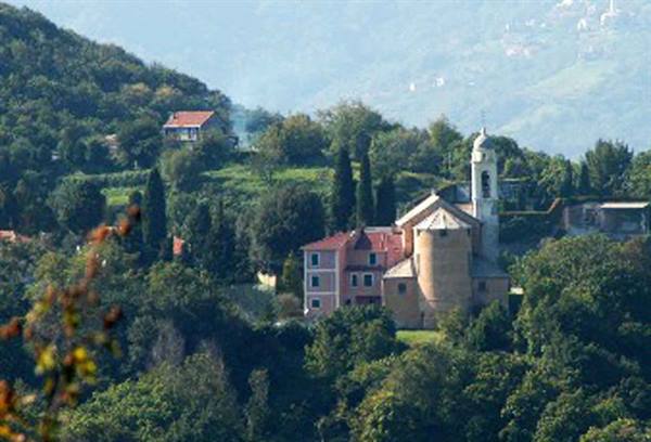 Church with bell tower among red houses on green hillside, hazy hills