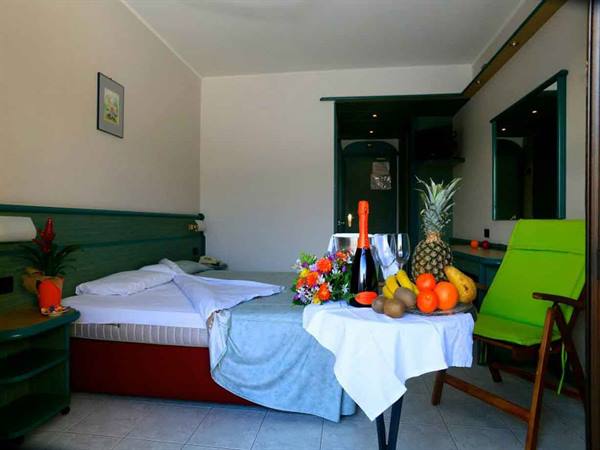 Hotel room with bed, sparkling wine bottle, tropical fruits and flowers