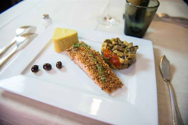 White plate with crispy salmon, polenta triangle and caponata, three olives