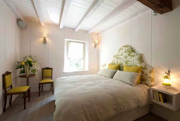 Bedroom with white wooden beams, double bed and yellow wooden chairs