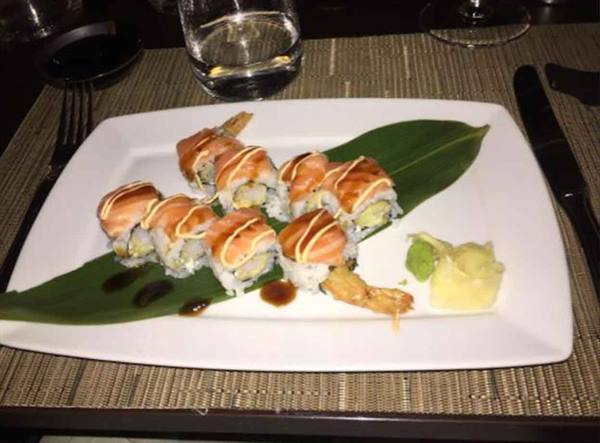 Salmon sushi rolls on green leaf with cutlery and glasses in restaurant