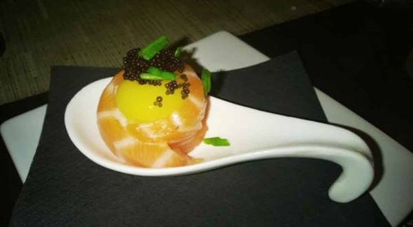 Smoked salmon with egg yolk and caviar on a white ceramic spoon