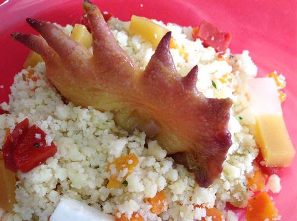 Roasted chicken foot on couscous with vegetables, pink plate under natural light
