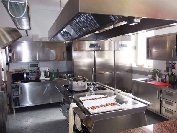 Stainless steel professional kitchen with hood, refrigerators and tray of pastries