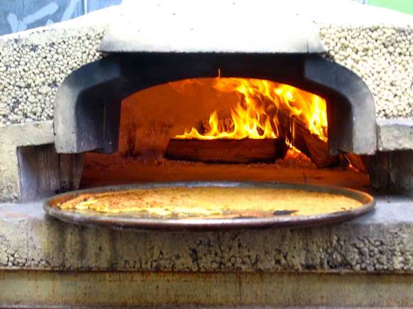 Wood-fired brick oven with orange flames and a pizza tray in front