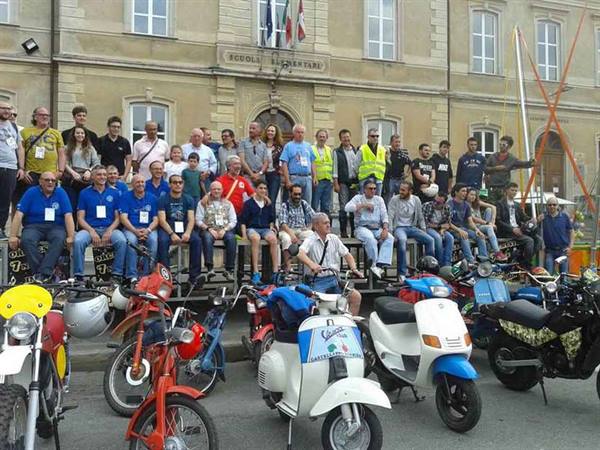 Vintage motorbike and scooter rally group posing in front of elementary school