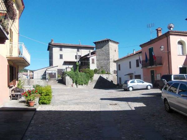 Cobblestone square with colorful houses, stone tower and parked cars under sun