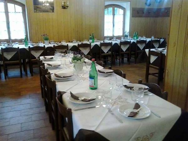Mountain refuge dining room with white tablecloths, glasses and green bottles set for dinner
