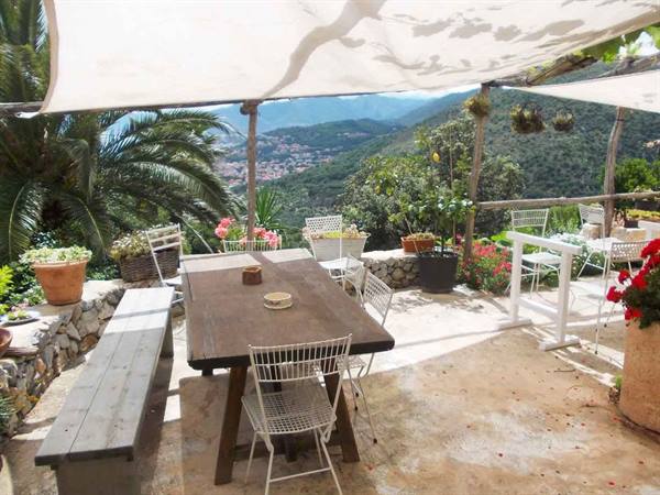 Wooden table under shade sails, terrace with flower pots and mountains
