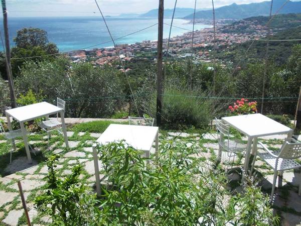 White tables on stone terrace, coastal town and turquoise sea beyond