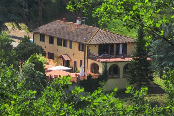 Yellow farmhouse with terracotta roof among trees, terrace with white umbrella
