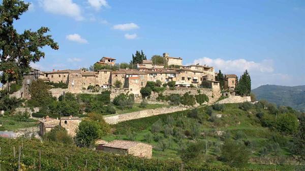 Stone medieval hilltop village surrounded by vineyards and olive groves under blue sky