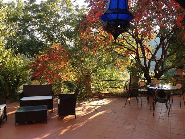 Terracotta terrace with rattan sofa, wrought-iron table and blue lantern among autumn trees