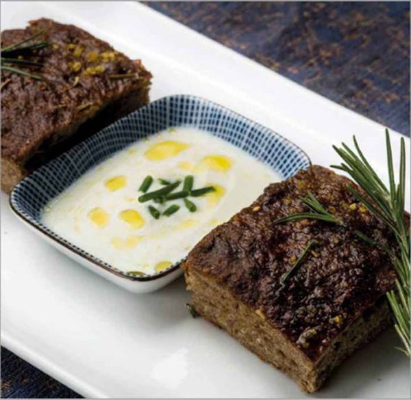 Meatloaf slices with rosemary and yogurt sauce on white plate