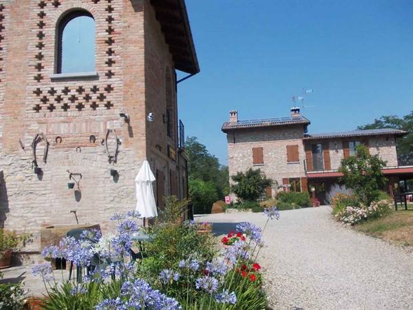 Brick farmhouse with purple flowers and gravel path under blue sky