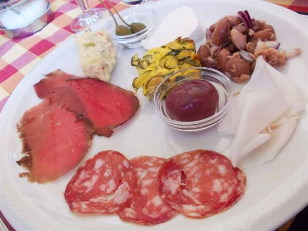Antipasto platter with roast beef, salami, beans, olives and lardo on checkered tablecloth