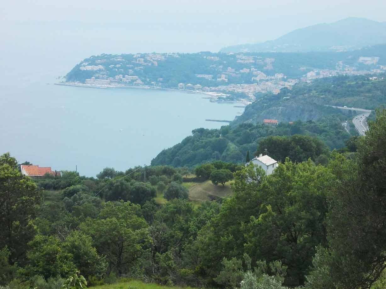 Costa ligure con baia, case tra gli alberi e autostrada sulla collina