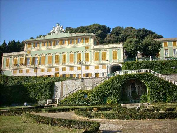Green villa with yellow windows, masonry staircases and hedges, blue sky
