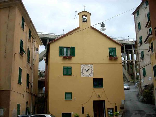 Small yellow church with clock and bell tower, concrete viaduct behind