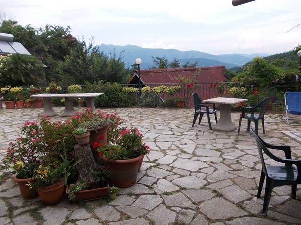 Stone terrace with geranium pots, tables and plastic chairs, cloudy mountains