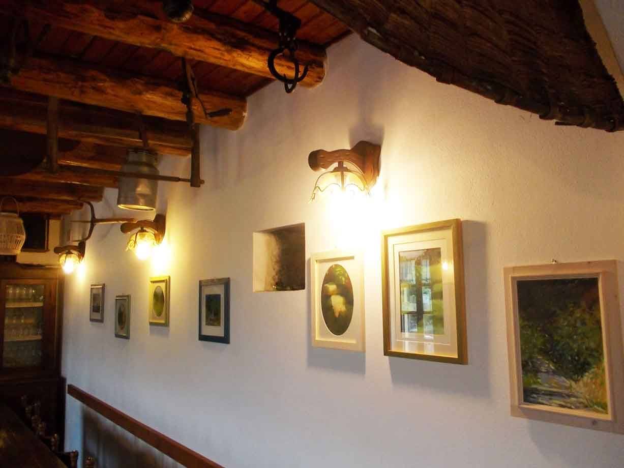 Quadri incorniciati su muro bianco sotto travi di legno e lampade accese