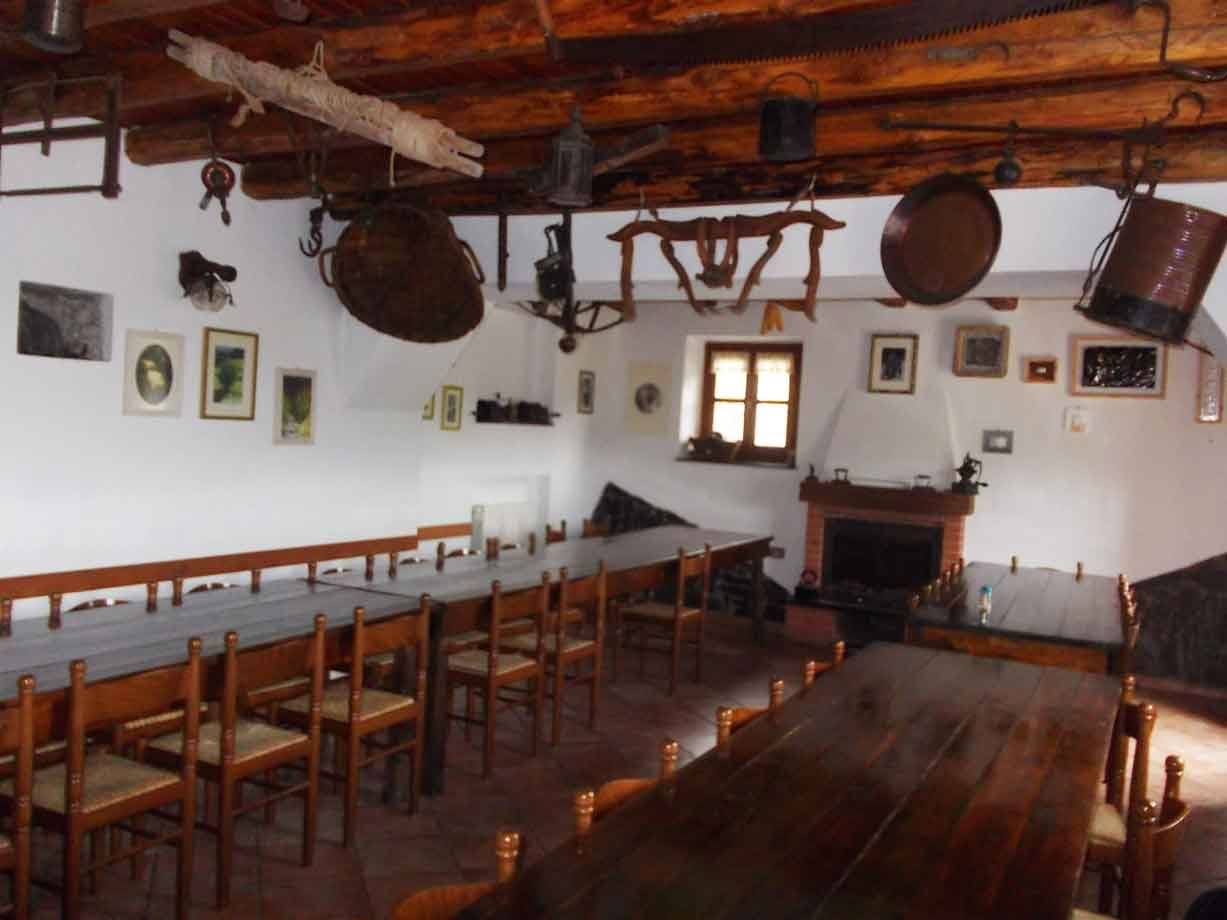 Sala rustica con tavoli in legno, travi e utensili d'epoca appesi al soffitto