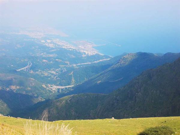 Highway viaducts winding through green mountains toward the coast and sea