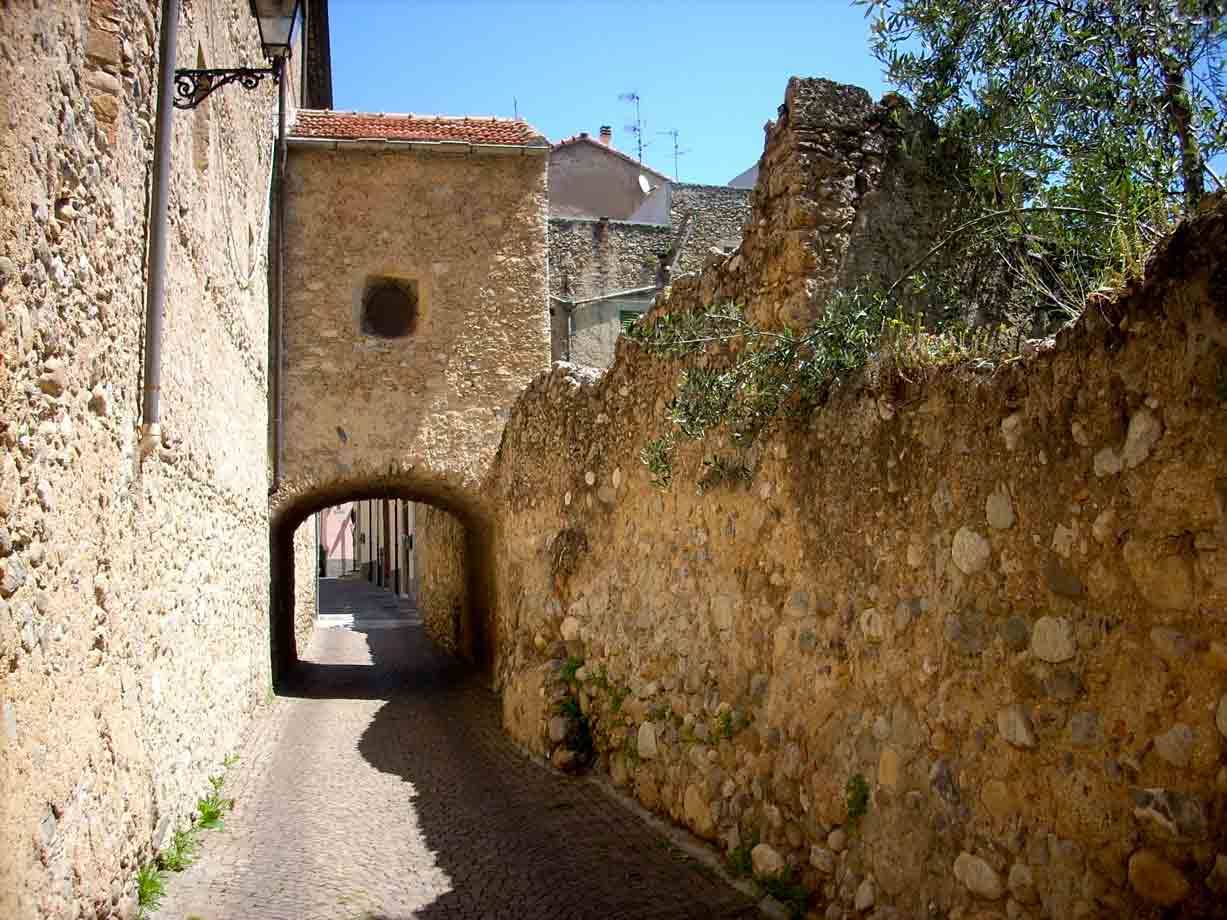 Vicolo in pietra con arco medievale e mura antiche sotto il sole